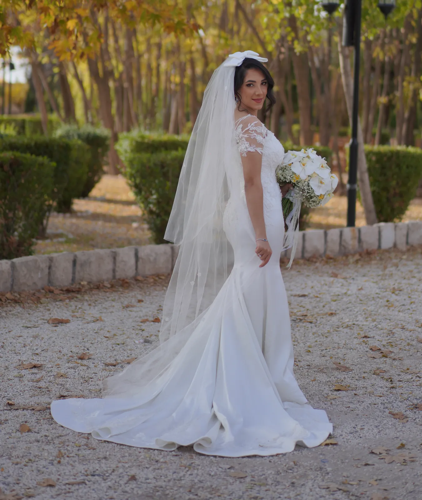 Custom mermaid wedding dress with lace sleeves and long veil, photographed outdoors